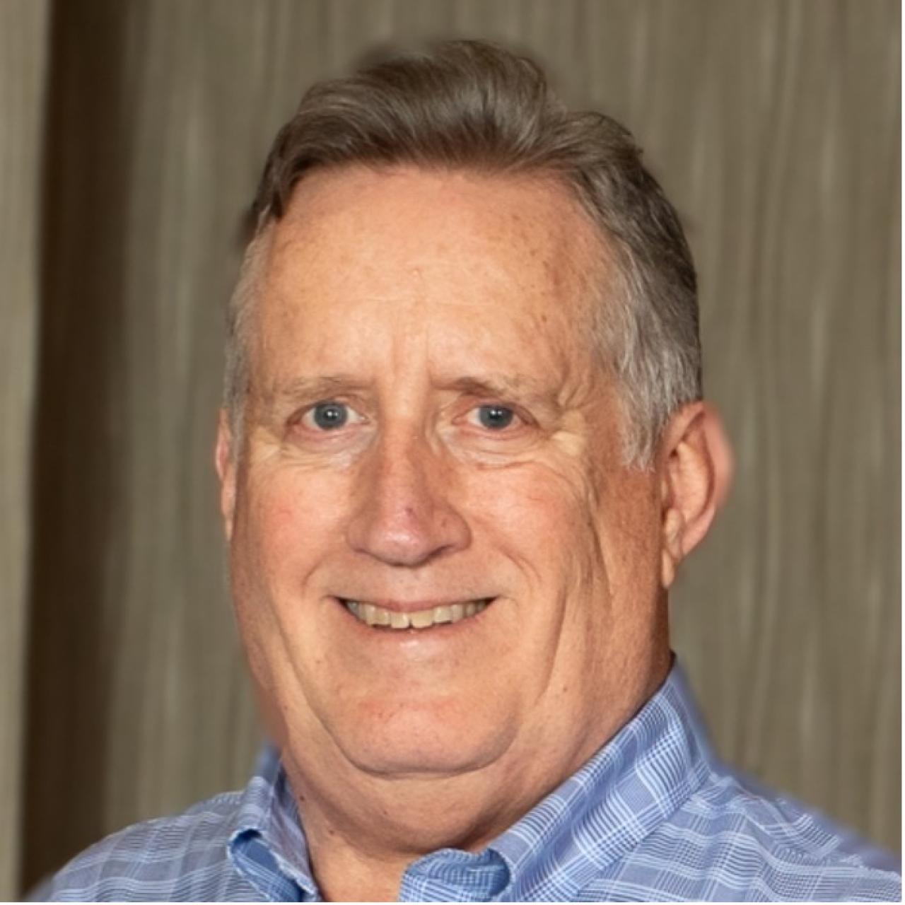 Mike Downing headshot wearing a blue shirt against wood grain background