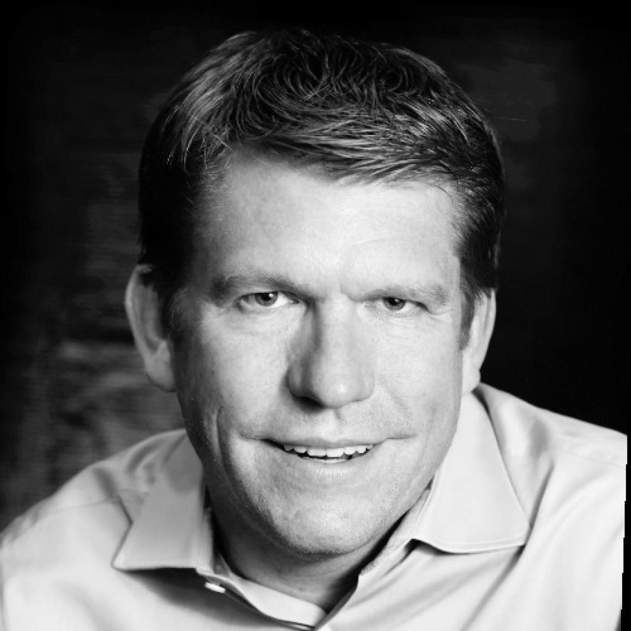 Black and white image of Matt looking into camera, wearing a collard shirt.