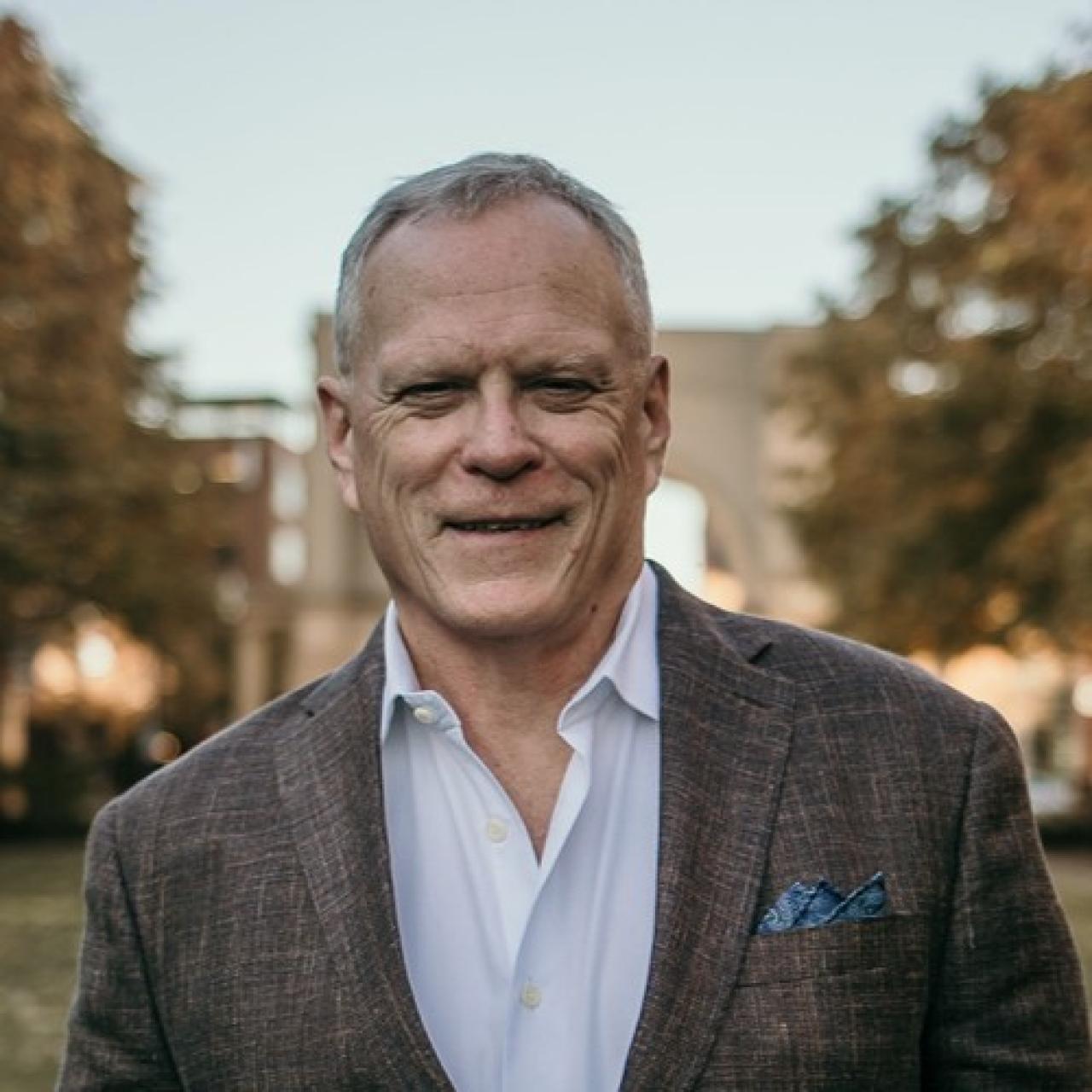 Brian wearing a sport coat and collared shirt with trees in the background.