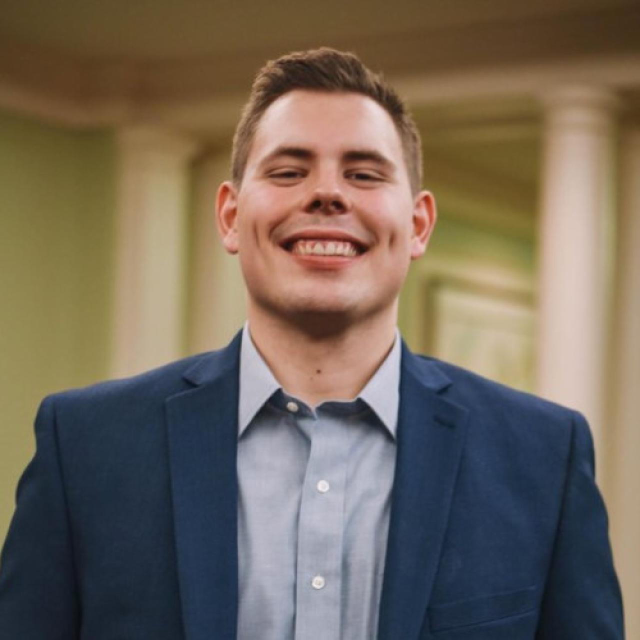 Cameron Little smiling wearing a blue suit jack and blue collared shirt