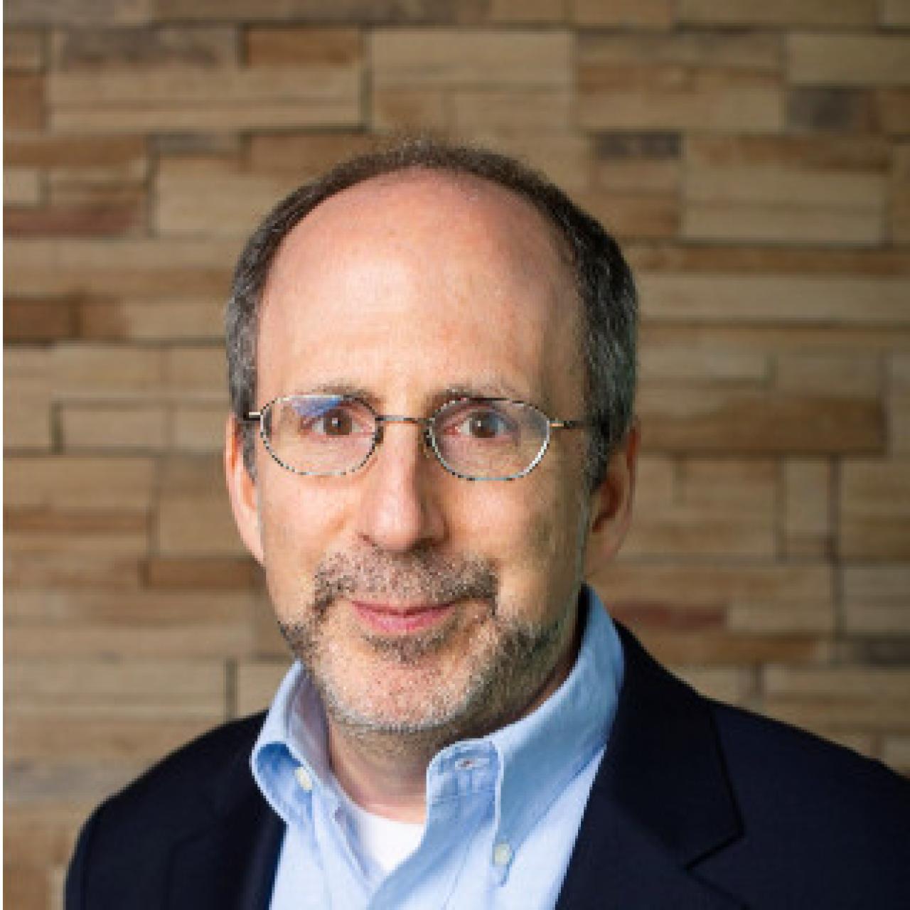 Michael standing against brick wall wearing light blue collared shirt.