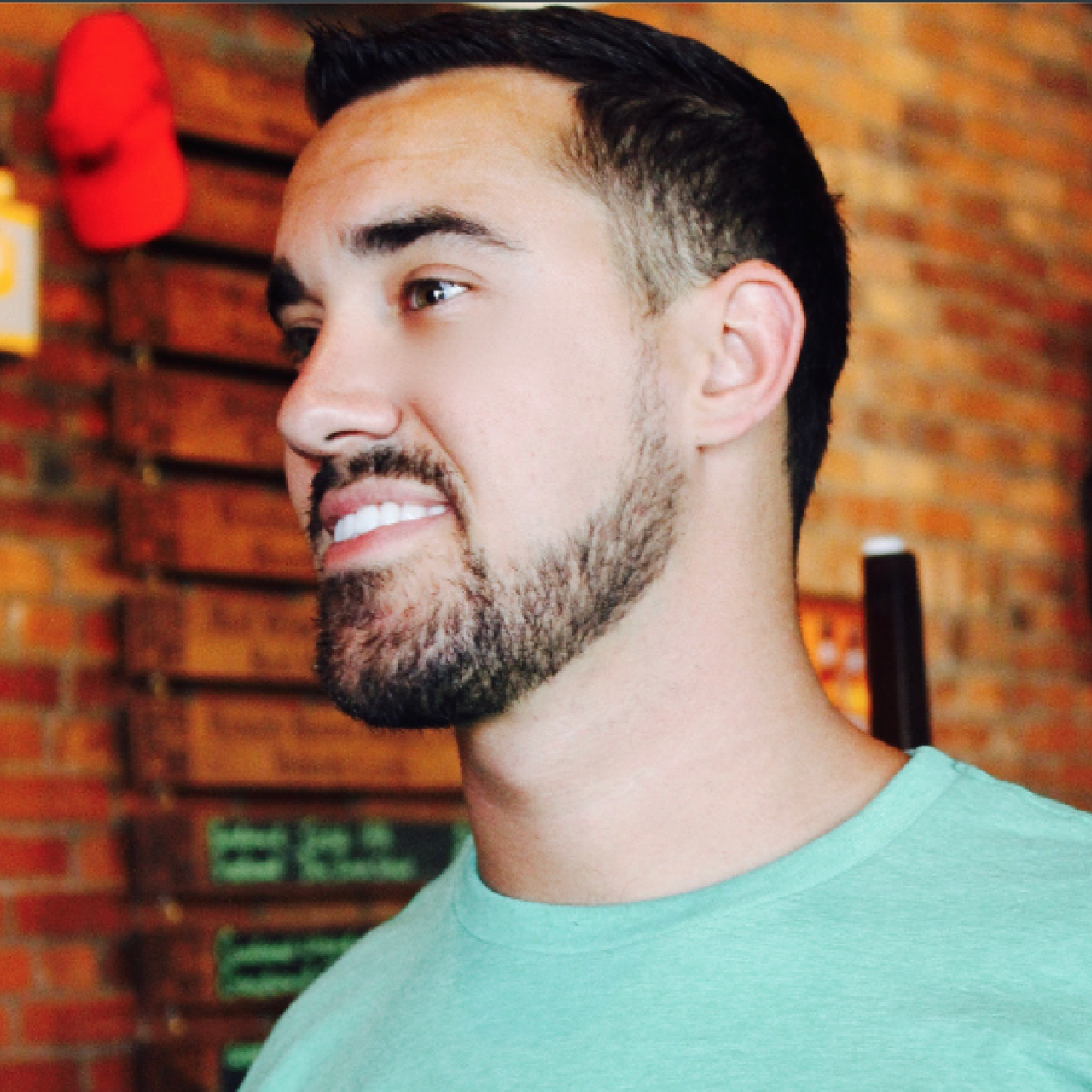 Trevor in a green shirt looking off to the side, standing in front of brick wall.