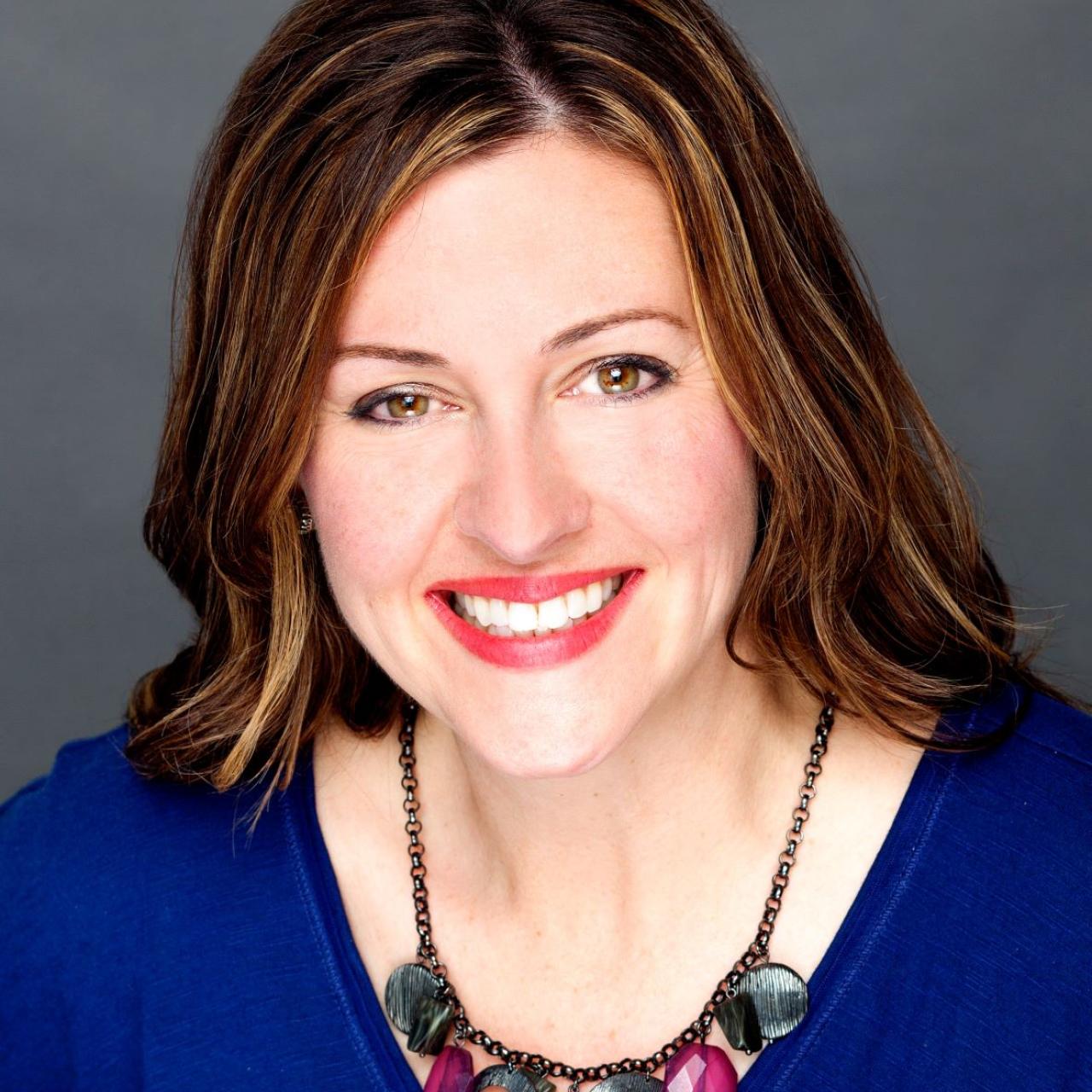 Jennifer Scheehle smiling, wearing blue top and jeweled necklace