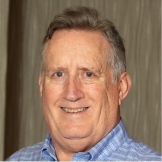 Mike Downing headshot wearing a blue shirt against wood grain background