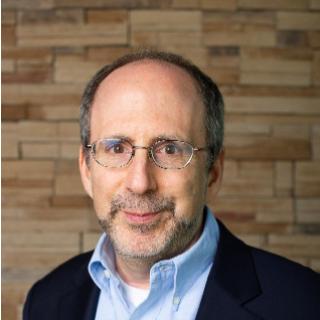 Michael standing against brick wall wearing light blue collared shirt.