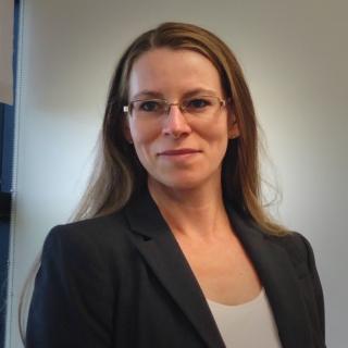 Erica in suit coat, standing in office.