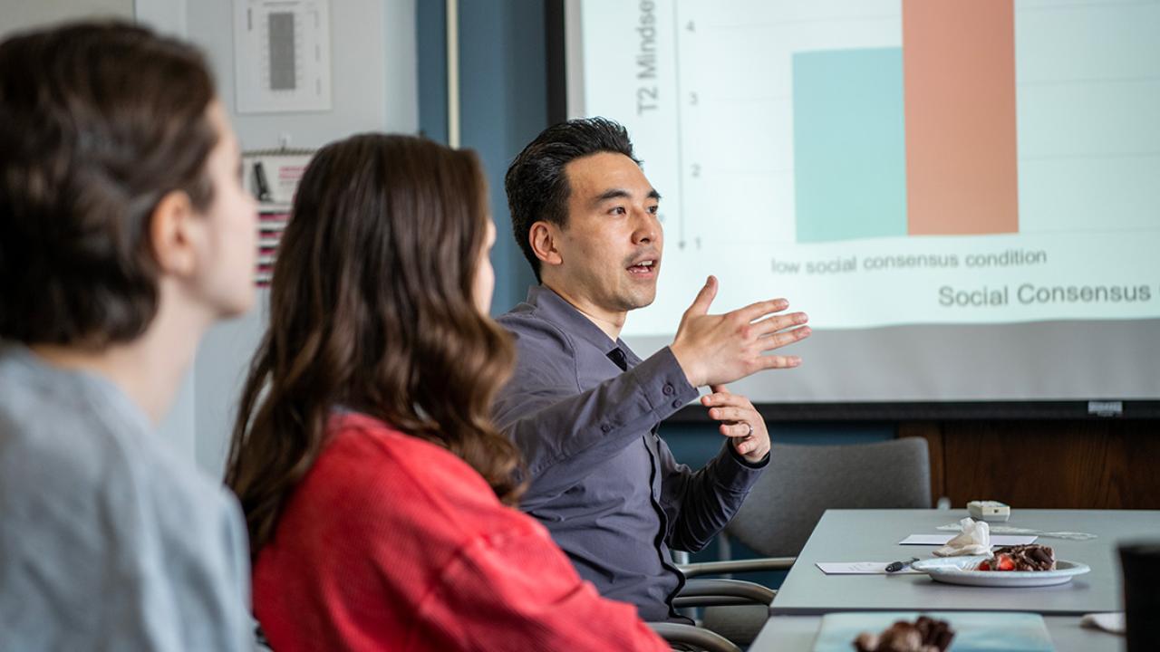 Man speaking and gesturing during meeting with slideshow statistics showing